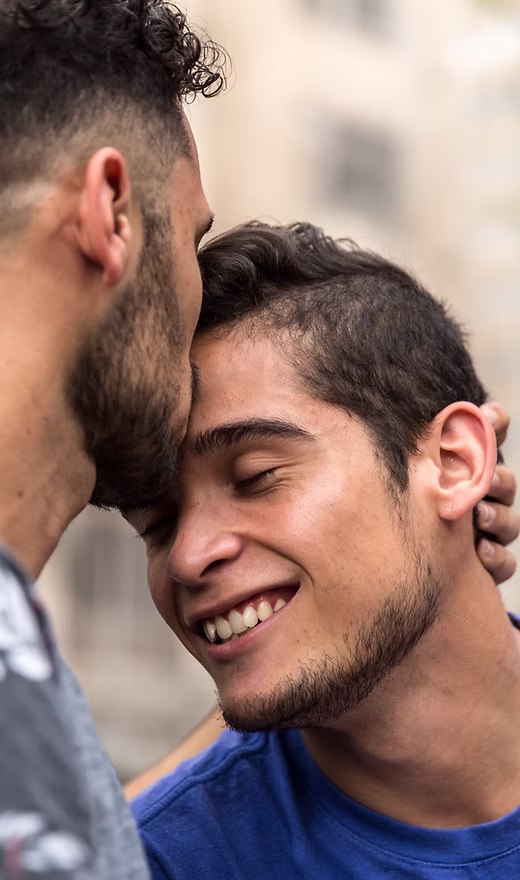 A man kissing his male partner on the forehead.